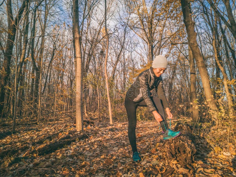 Autumn fall outdoor training running athlete woman on trail run getting ready jogging tying shoe laces outside forest