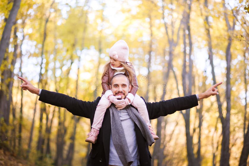 Autumn fashion for children and the whole family. A small daughter sits on the shoulders of the father in the neck against the bac stock photo Autumn fashion for children and the whole family. A small daughter sits on the shoulders of the father in the neck against the bac stock photo