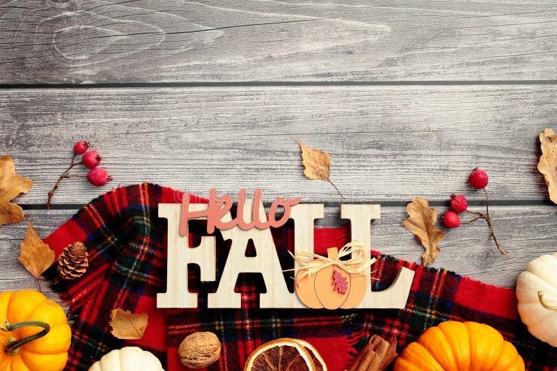 Autumn flat lay composition. Red plaid with pumpkins, red berries, dry leaves, nuts, Hello Fall sign on wooden desk table. Flat stock photos