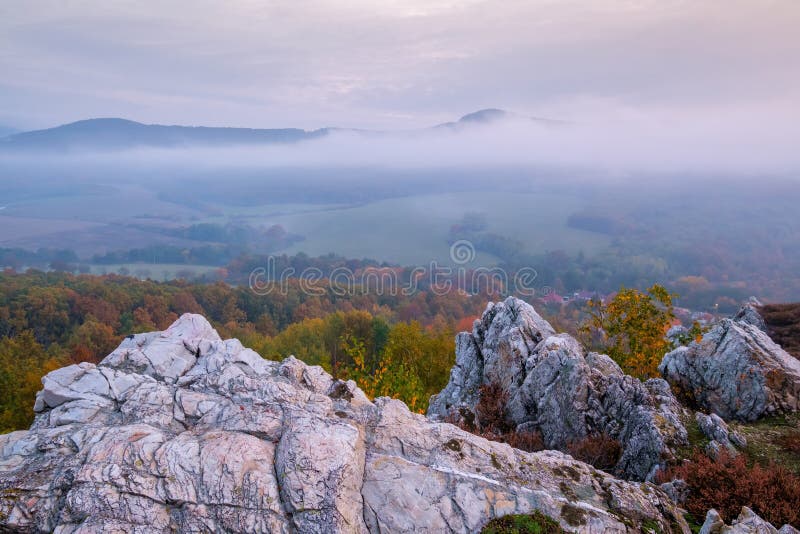 Autumn forest landscape among large rocks with view of mountain misty valley and colorful autumn forest.