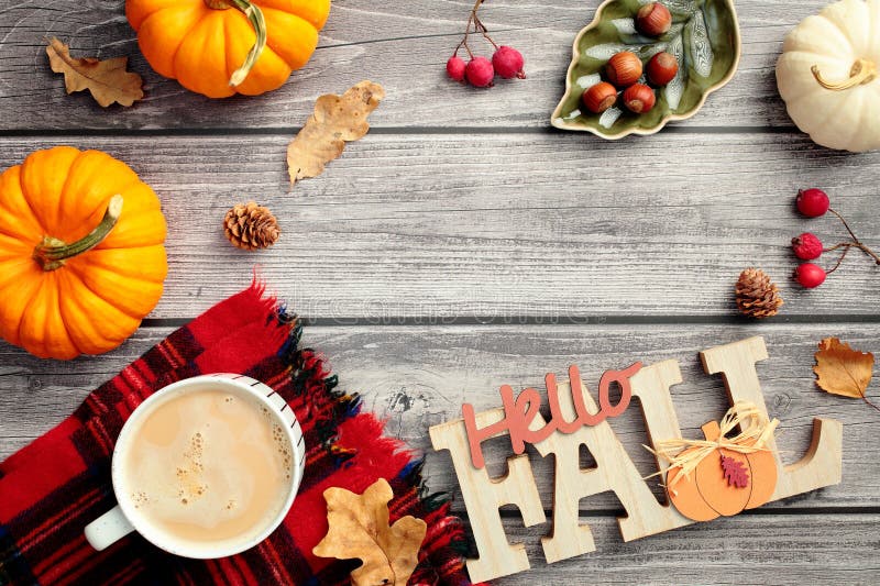 Autumn frame. Hello Fall sign, red berries, fall leaves, pumpkins, coffee cup on red plaid on wooden desk table. Flat lay, top stock photo