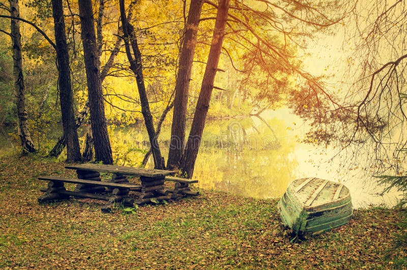 Autumn lake in golden sunlight. Golden sunlight shining over wooded shoreline of lake with upturned boat, autumn scene stock image Autumn lake in golden sunlight. Golden sunlight shining over wooded shoreline of lake with upturned boat, autumn scene stock image