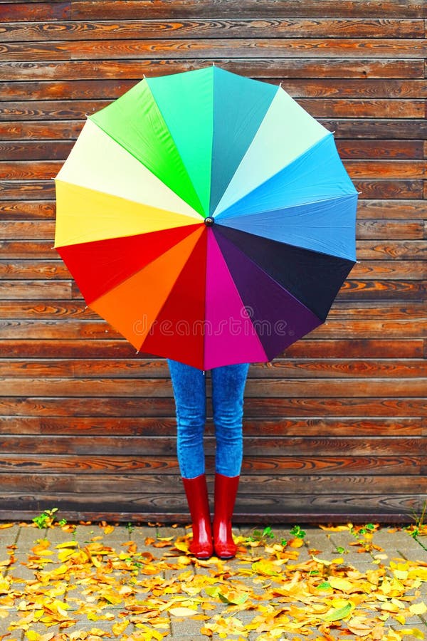 Autumn photo woman holding colorful umbrella wearing a red rubber boots over wooden background yellow leafs