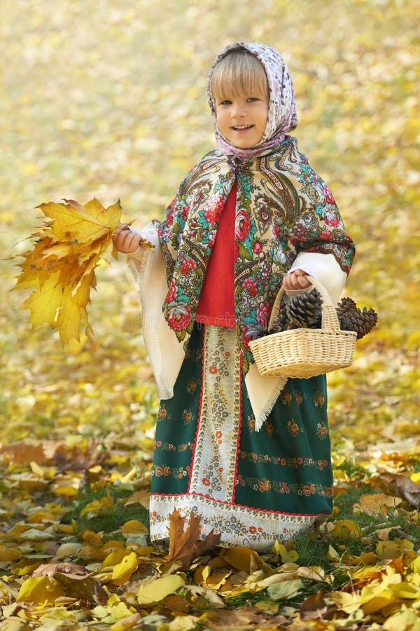 Autumn portrait of the little girl in the traditional russian sarafan and headscarf gathering yellow leaves and pinecones royalty free stock images Autumn portrait of the little girl in the traditional russian sarafan and headscarf gathering yellow leaves and pinecones royalty free stock images