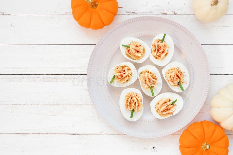 Autumn pumpkin theme deviled eggs. Top view table scene on a white wood background with copy space. stock photos