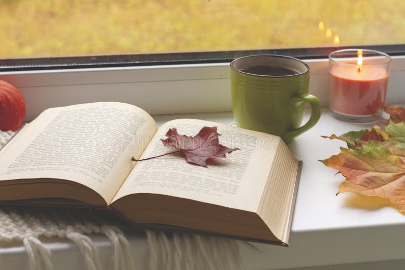 Autumn still life. books, leaves, cup and candlestick on window.