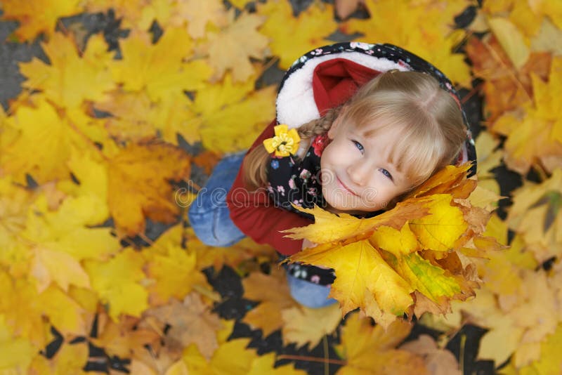 Autumn street portrait of the little girl holding a bunch of maple leaves