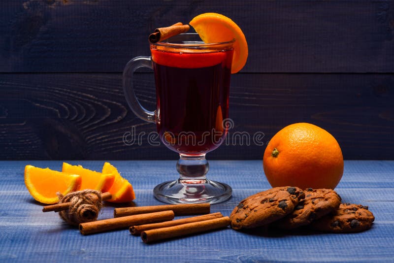 Autumn treats concept. Glass with mulled wine near orange fruit on dark background. Drink or beverage with cinnamon. Sticks, orange fruit and cookies with royalty free stock photography Autumn treats concept. Glass with mulled wine near orange fruit on dark background. Drink or beverage with cinnamon. Sticks, orange fruit and cookies with royalty free stock photography