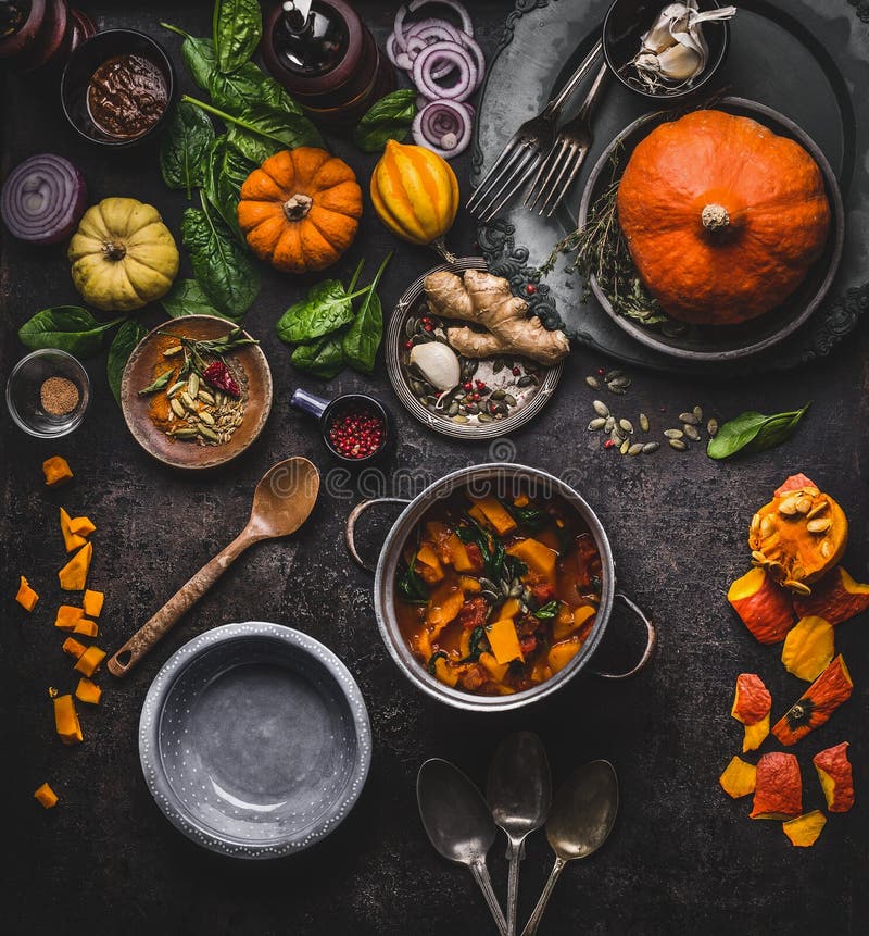 Autumn and winter cooking and eating with pumpkin dishes. Vegetarian stew in cooking pot with spoon and vegetables ingredients on