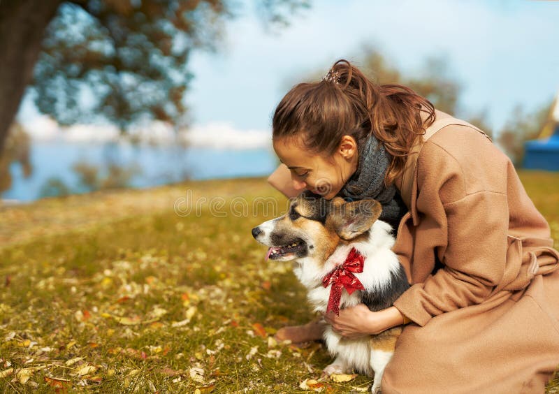 Autumn woman in coat tenderly embracing Welsh Corgi dog in autumn park, cute moments with pet.