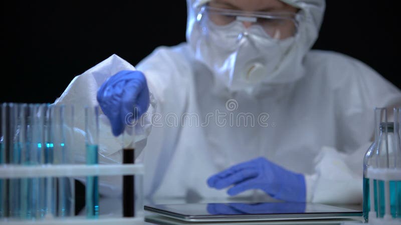 Auxiliar de laboratorio en traje protector estudiando muestras de aceite lÃ­quido para la fabricaciÃ³n de notas