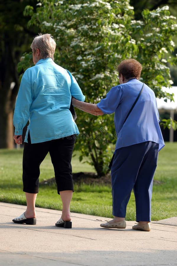 A woman assist her elderly mother as they walk. A woman assist her elderly mother as they walk.