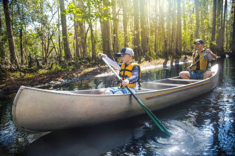 Adventuresome Father and son canoeing together on a beautiful river in a thick forest. Family vacations and new experiences. Smiling and having fun together in nature. Adventuresome Father and son canoeing together on a beautiful river in a thick forest. Family vacations and new experiences. Smiling and having fun together in nature