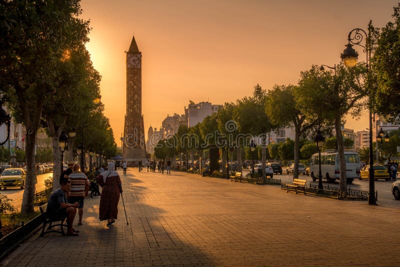 The Avenue Habib Bourguiba Clocktower in Tunis downtown, the famous landmark of Tunisia, with the people walking by on promenade during the colorful sunset. The Avenue Habib Bourguiba Clocktower in Tunis downtown, the famous landmark of Tunisia, with the people walking by on promenade during the colorful sunset.