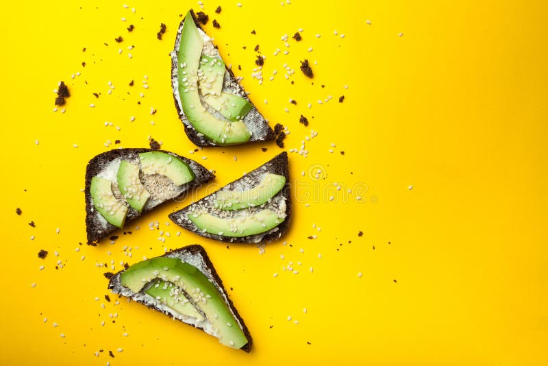 Avocadotoost op een gele achtergrond, een zwarte brood en plakken van rijpe avocado met kaas royalty-vrije stock afbeeldingen Avocadotoost op een gele achtergrond, een zwarte brood en plakken van rijpe avocado met kaas royalty-vrije stock afbeeldingen