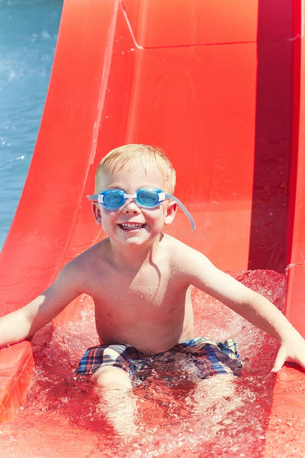 A cute little boy smiling after sliding down a water slide at an outdoor waterpark. A cute little boy smiling after sliding down a water slide at an outdoor waterpark