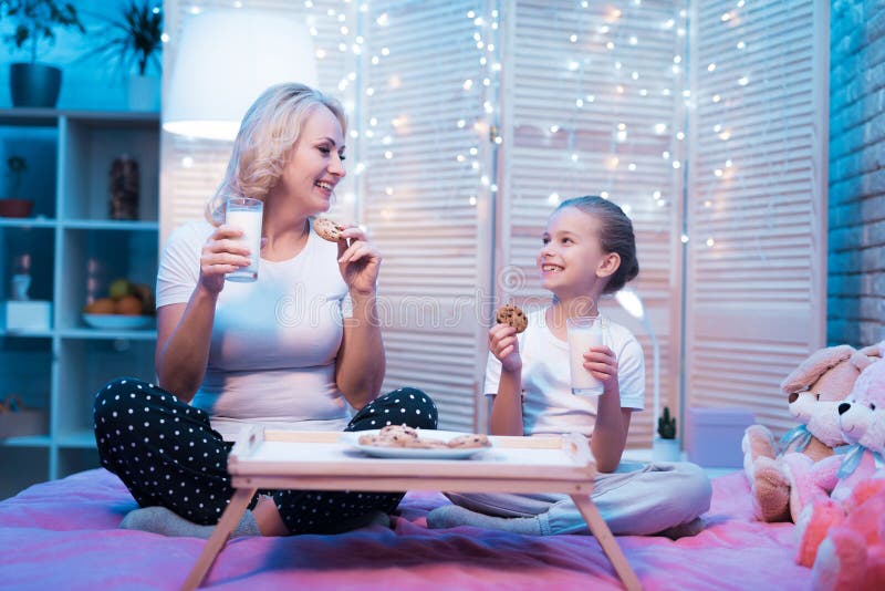 A avó e a neta estão comendo cookies com leite na noite em casa imagens de stock A avó e a neta estão comendo cookies com leite na noite em casa imagens de stock