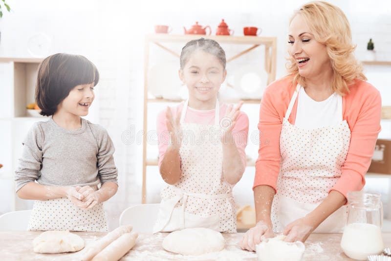 A avó nova com netos pequenos está rindo na cozinha Cookies do cozimento imagem de stock A avó nova com netos pequenos está rindo na cozinha Cookies do cozimento imagem de stock