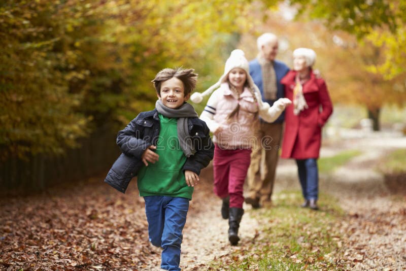 Avós com os netos que correm ao longo de Autumn Path