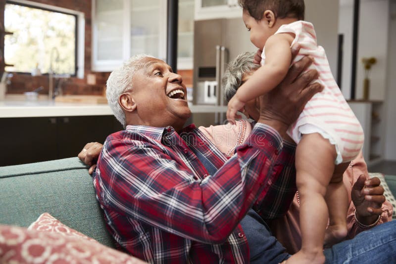 Avós que sentam-se em Sofa Playing With Baby Granddaughter em casa imagem de stock royalty free Avós que sentam-se em Sofa Playing With Baby Granddaughter em casa imagem de stock royalty free