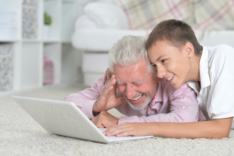 Avô com neto usando laptop deitado no chão imagem de stock