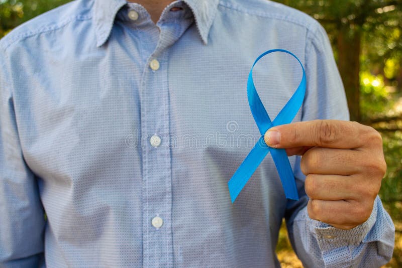 Awareness of prostate cancer, a man holding a light blue ribbon on a background of autumn leaves. To support people living with an stock photos Awareness of prostate cancer, a man holding a light blue ribbon on a background of autumn leaves. To support people living with an stock photos