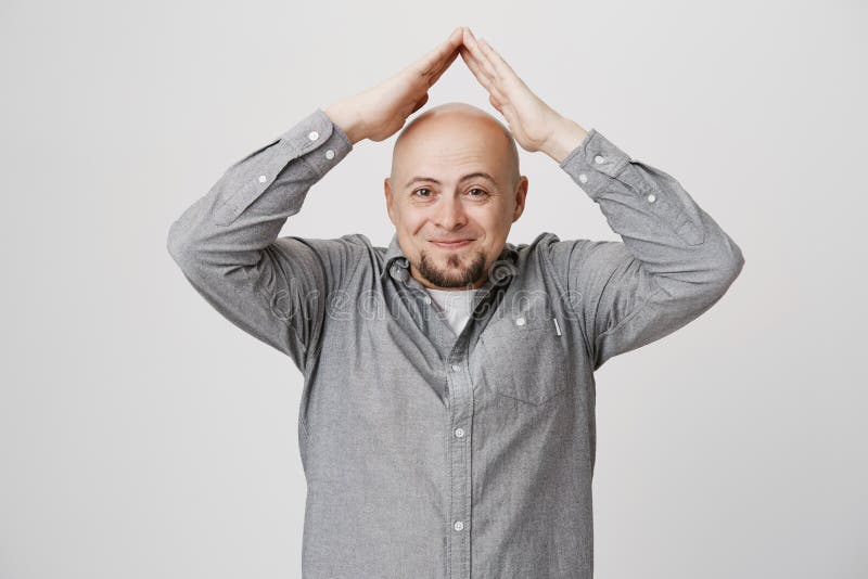 Awkwardly smiling bearded guy holding his hands above head imitating roof gesture over white background. Male tries to explain his coworkers he has lot of work to do, he can not help arrange party.