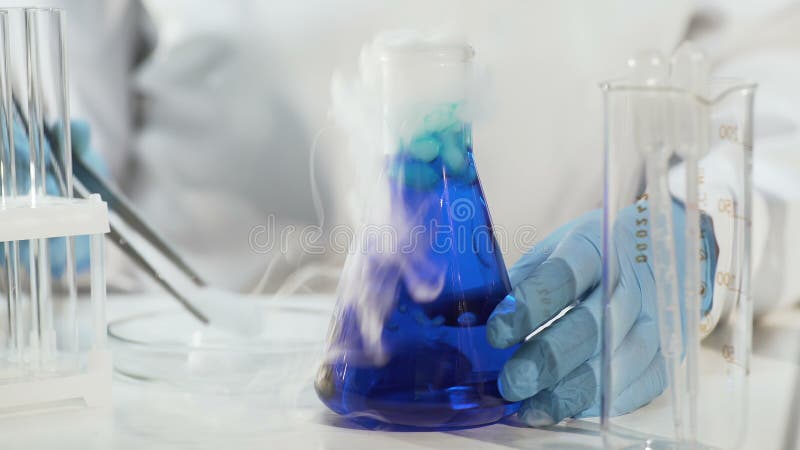 Ayudante de laboratorio que pone el hielo seco en líquido azul en el frasco cónico, haciendo que hierve