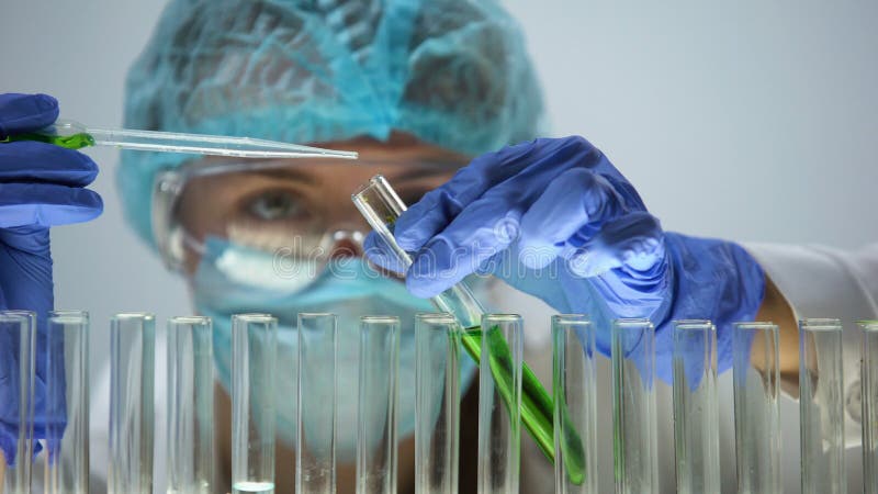 Ayudante de laboratorio que vierte el líquido verde en el tubo de ensayo, productos orgánicos