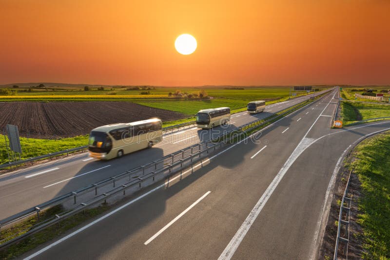Ayunan los autobuses del viaje en fila en la carretera en la puesta del sol fotografía de archivo Ayunan los autobuses del viaje en fila en la carretera en la puesta del sol fotografía de archivo