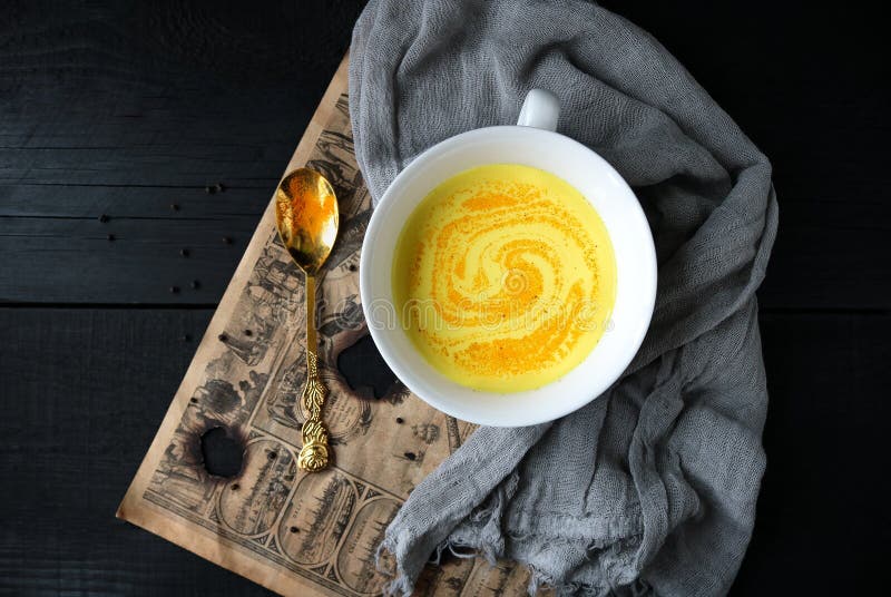 Ayurvedic drink. Moon milk with turmeric for better sleep in a white cup on a black background.
