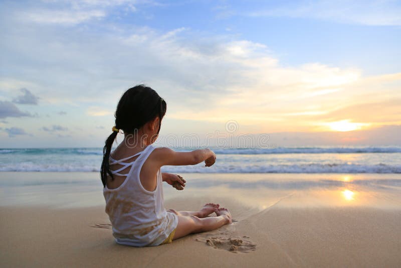 Aziatisch meisje zitting en het spelen zand op het strand bij de zonsondergang stock afbeeldingen Aziatisch meisje zitting en het spelen zand op het strand bij de zonsondergang stock afbeeldingen