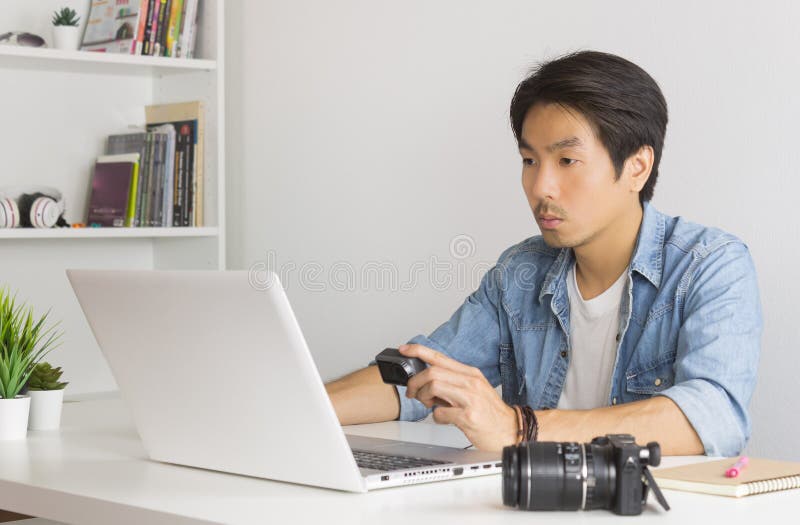 Aziatische fotograaf of freelancer die Dossier in Action Camera met Laptop in het Bureau van het Huis controleert stock afbeelding Aziatische fotograaf of freelancer die Dossier in Action Camera met Laptop in het Bureau van het Huis controleert stock afbeelding