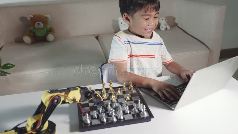 Aziatische kleine jongen programmeert code voor robotarm op laptop voor spelschacht