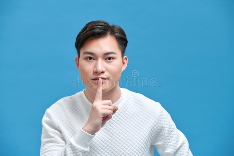 Portrait of serious young Asian man showing a sign of silence gesture putting fingers in mouth. Portrait of serious young Asian man showing a sign of silence gesture putting fingers in mouth