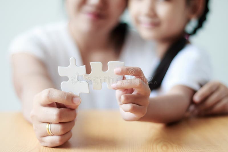 Asian little girl playing jigsaw puzzle with her mother for family concept shallow depth of field select focus on hands. Asian little girl playing jigsaw puzzle with her mother for family concept shallow depth of field select focus on hands