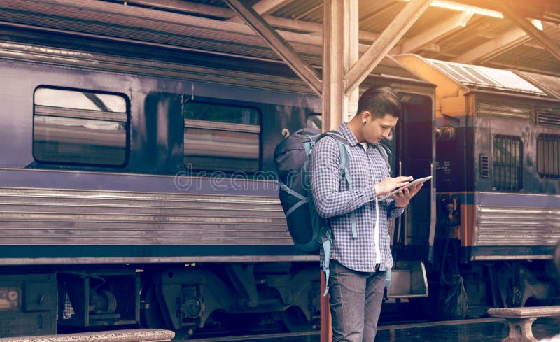 Aziatische mensenrugzak voor reis bij station en het gebruiken van tablet stock fotografie Aziatische mensenrugzak voor reis bij station en het gebruiken van tablet stock fotografie