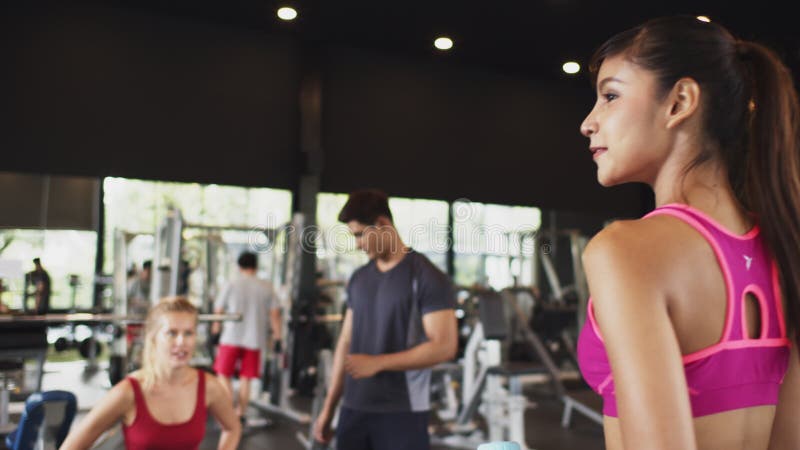 Aziatische vrouw begroet Kaukasische vriend die oefent met mannelijke persoonlijke trainer in fitnessgym of sportclub Recreatie