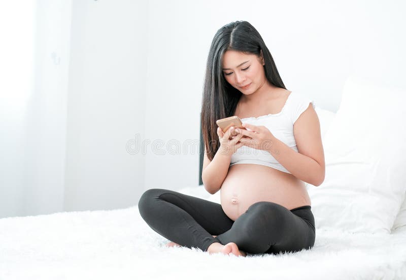 Aziatische zwangere vrouw gebruikt haar mobiele telefoon om te kijken naar wat nieuws over het zoeken naar de kennis over babyver royalty-vrije stock afbeeldingen Aziatische zwangere vrouw gebruikt haar mobiele telefoon om te kijken naar wat nieuws over het zoeken naar de kennis over babyver royalty-vrije stock afbeeldingen