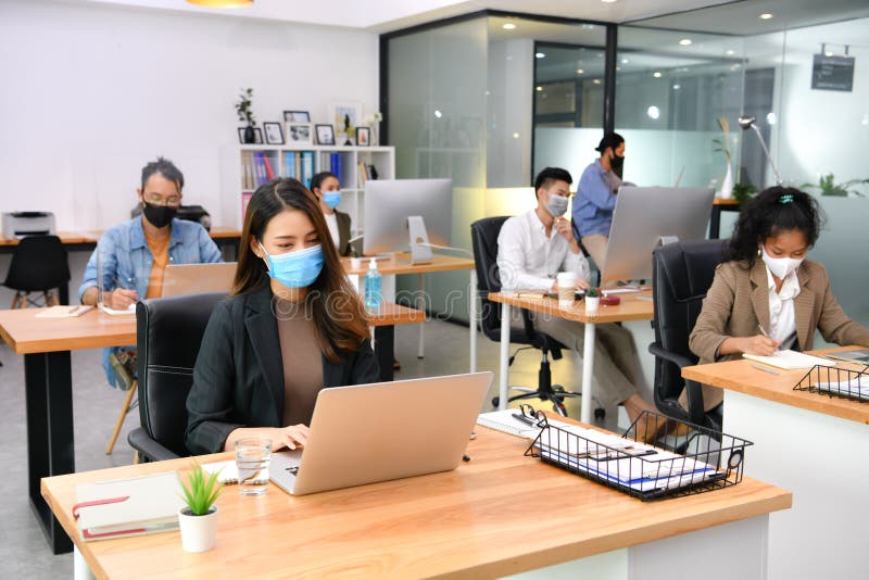 Asian office workers wearing face masks working in new normal office and doing social distancing during corona virus covid-19 pandemic. Asian office workers wearing face masks working in new normal office and doing social distancing during corona virus covid-19 pandemic