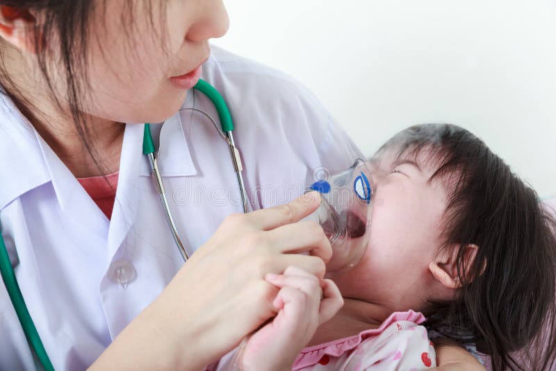 Closeup asian child having respiratory illness helped by doctor with inhaler. Pediatrician take care girl with asthma problems making inhalation with mask at hospital. child was bronchitis and crying. Closeup asian child having respiratory illness helped by doctor with inhaler. Pediatrician take care girl with asthma problems making inhalation with mask at hospital. child was bronchitis and crying.