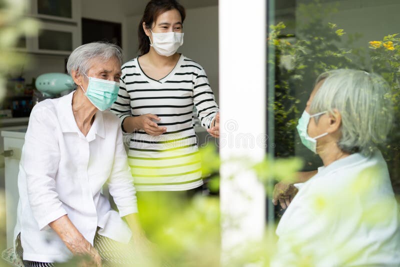 Asian woman and old elderly with medical masks on the face,daughter talking happily visited her senior mother at home,wear a protective face mask for safety while close to each other,New normal life. Asian woman and old elderly with medical masks on the face,daughter talking happily visited her senior mother at home,wear a protective face mask for safety while close to each other,New normal life