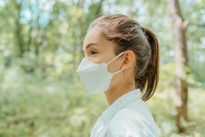 Asian woman wearing face mask walking in outdoor nature. Eco-friendly sustainable masks concept. Woman with korean kn95 mouth covering for corona virus prevention in forest. Asian woman wearing face mask walking in outdoor nature. Eco-friendly sustainable masks concept. Woman with korean kn95 mouth covering for corona virus prevention in forest.