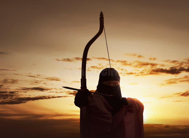 Asian muslim woman wearing hijab holding bow to shoot an arrow against sunset background. Asian muslim woman wearing hijab holding bow to shoot an arrow against sunset background