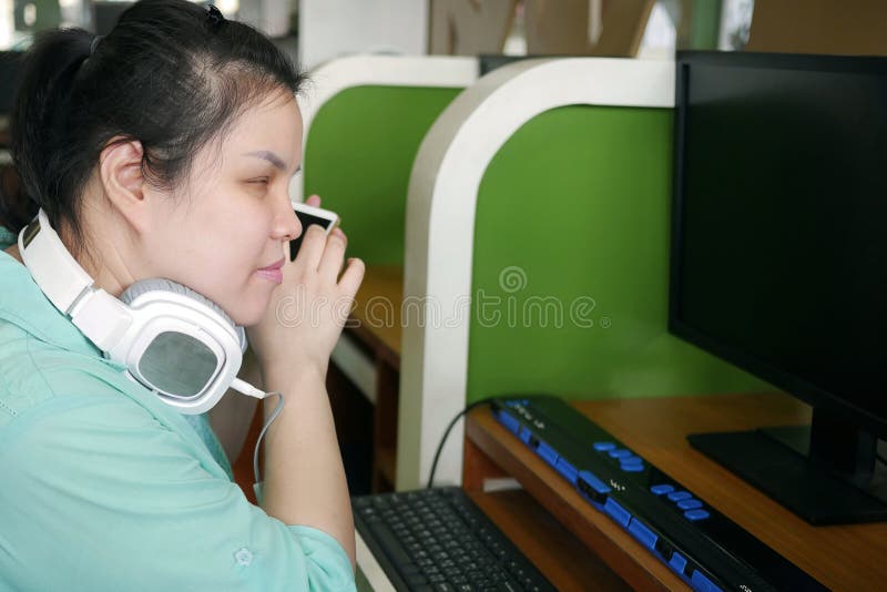 Azjatycka młoda niewidoma kobieta z słuchawką korzystająca z smartfonu z technologią wspomagania głosowego dla osób niepełnosprawn