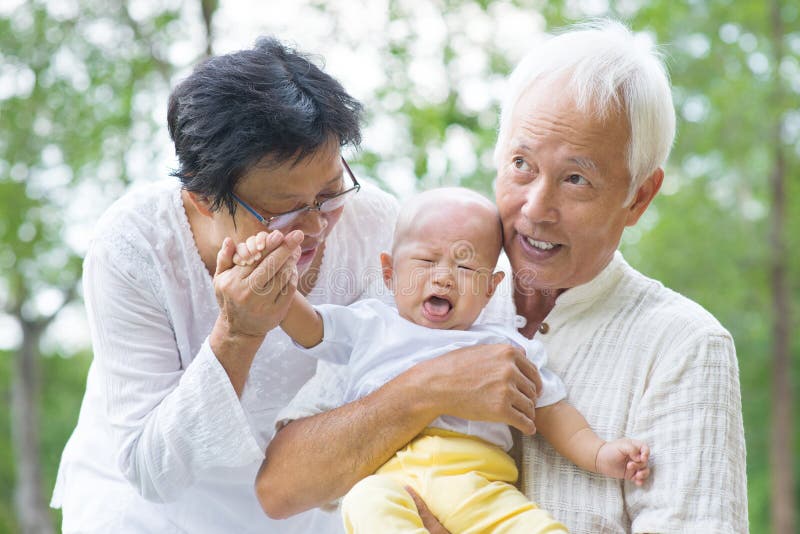 Asian crying baby comforted by grandparents at outdoor garden. Asian crying baby comforted by grandparents at outdoor garden