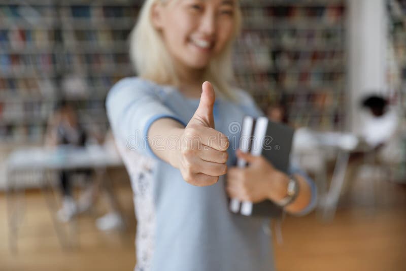Azjatycka studentka stojąca w bibliotece pokazująca zbliżenie kciuka zdjęcia stock