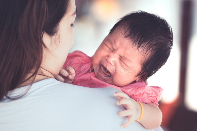 Cute asian newborn baby girl crying with tried on mother`s shoulder.Young mother cuddling baby with tenderness. Cute asian newborn baby girl crying with tried on mother`s shoulder.Young mother cuddling baby with tenderness.