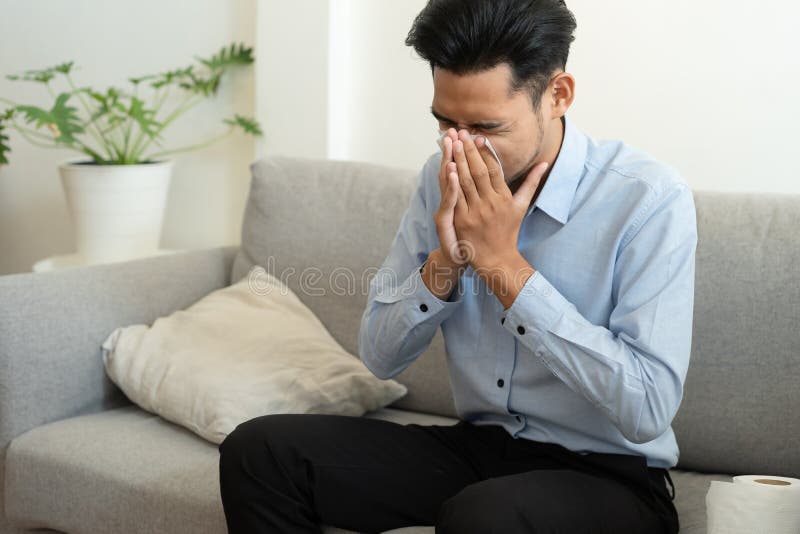 Azjatycki przystojniak człowieka, który ma sezon grypowy i kichał przy użyciu papierowych tkanek siedzących na kanapie w domu konc