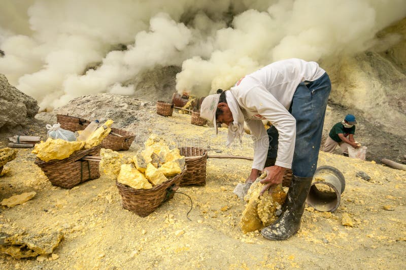 Azufre en Kawah Ijen. Kawah Ijen, Indonesia - abril 24,2010: Trabajadores que extraen el azufre dentro del cráter de Ijen en el volcán de Ijen, Indonesia Él lleva la carga alrededor de 60kg al top del rasgón y entonces los 3km abajo